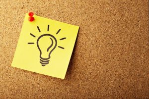 A lightbulb drawn on a sticky note is pinned to a corkboard.